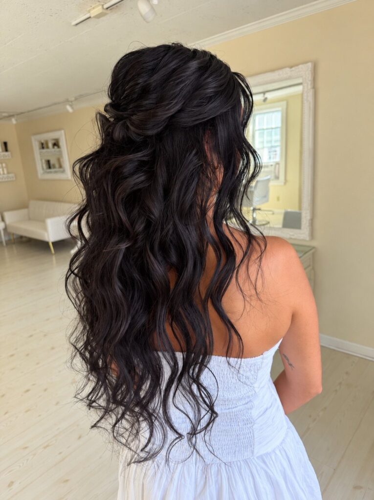 Woman with long wavy black hair in a half-up bridal hairstyle wearing white.