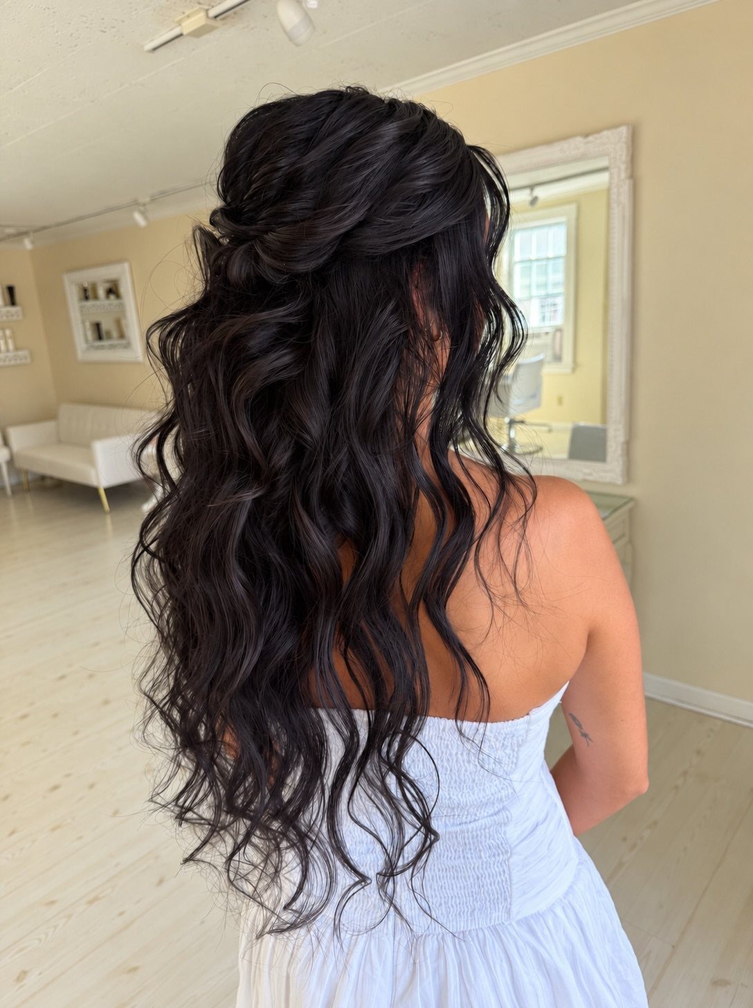 Woman with long wavy black hair in a half-up bridal hairstyle wearing white.