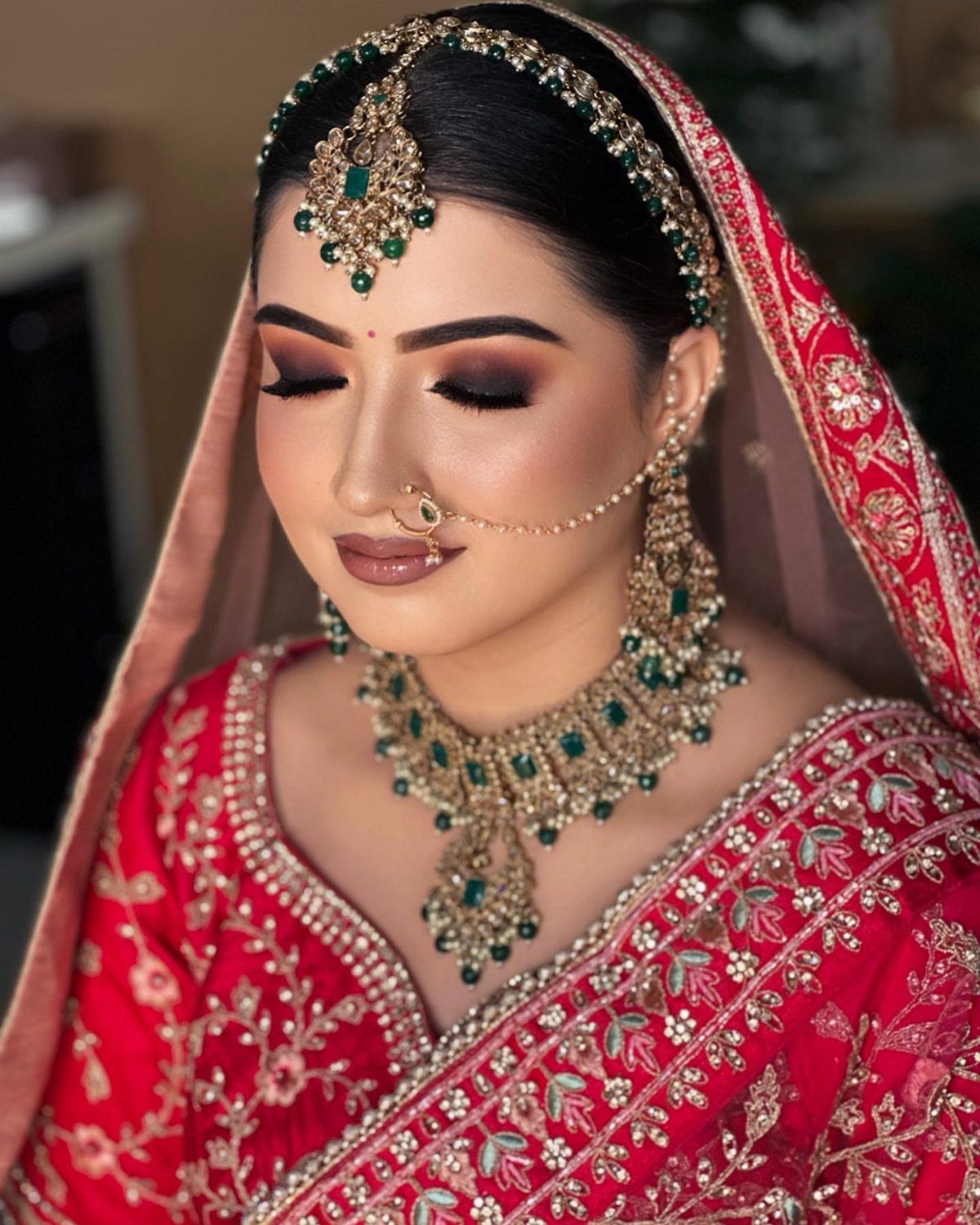 Bride with dark smokey eye makeup wearing traditional red Indian bridal clothing and jewelry