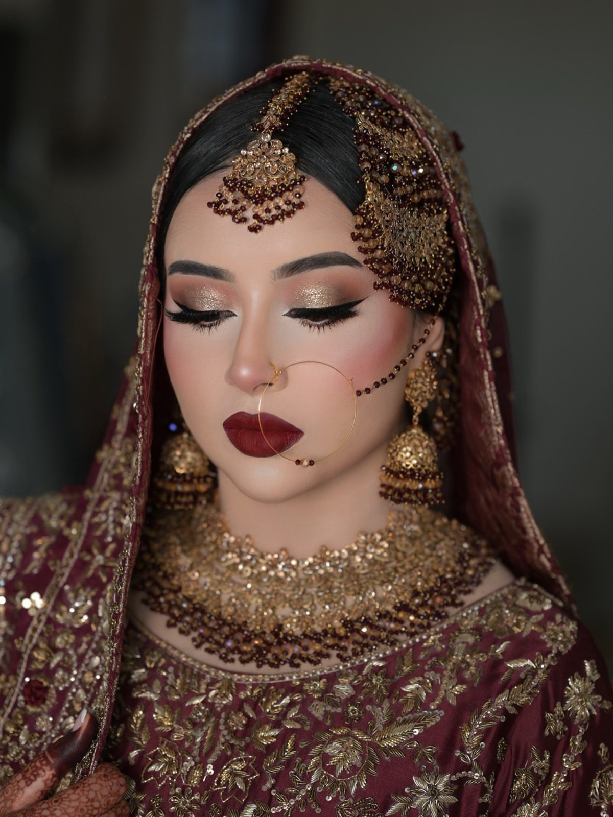 Bride with gold eyeshadow and red lips wearing traditional maroon bridal attire and jewelry