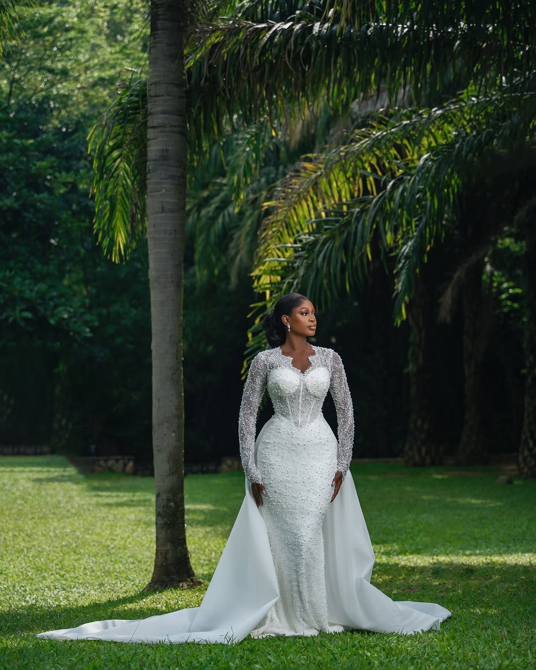 Bride in a white lace wedding gown posing in a tropical garden setting