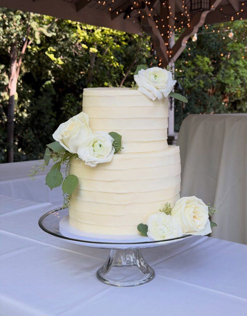 Two-tier white buttercream wedding cake with horizontal ridges and fresh white roses.