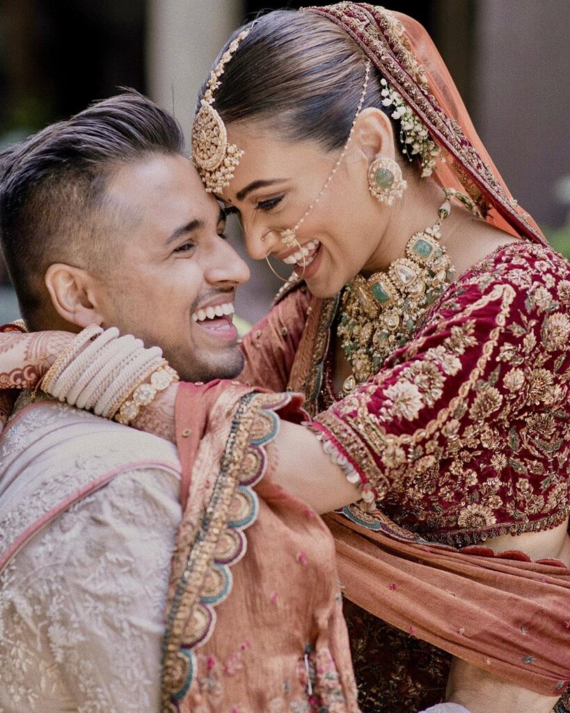 Smiling couple in traditional Indian wedding attire embracing and looking at each other.