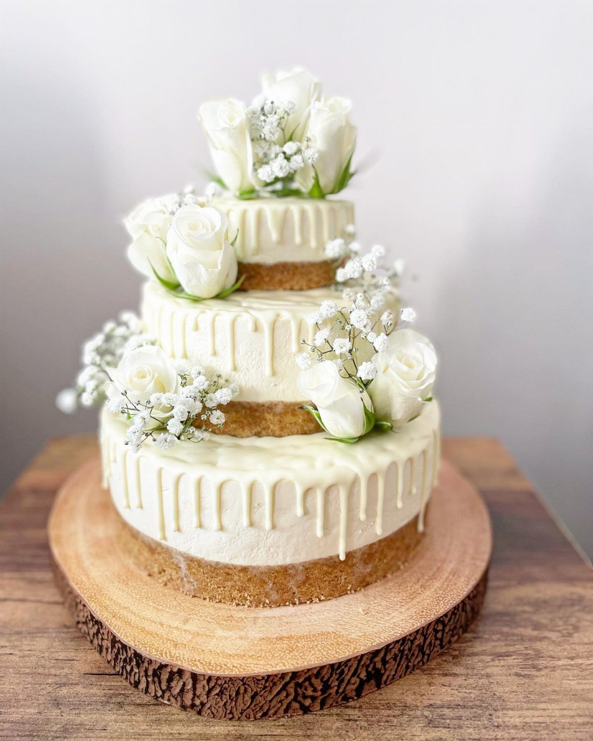 Three-tiered white cheesecake wedding cake with white roses on a wooden platter