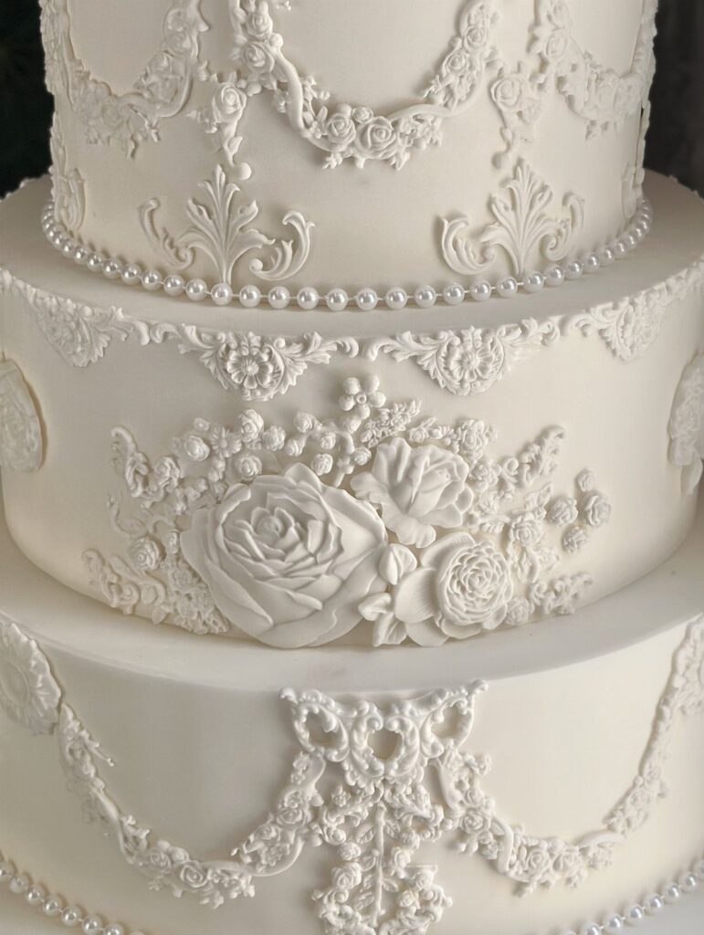 White multi-tiered wedding cake with intricate frosting lace and sculpted sugar roses.