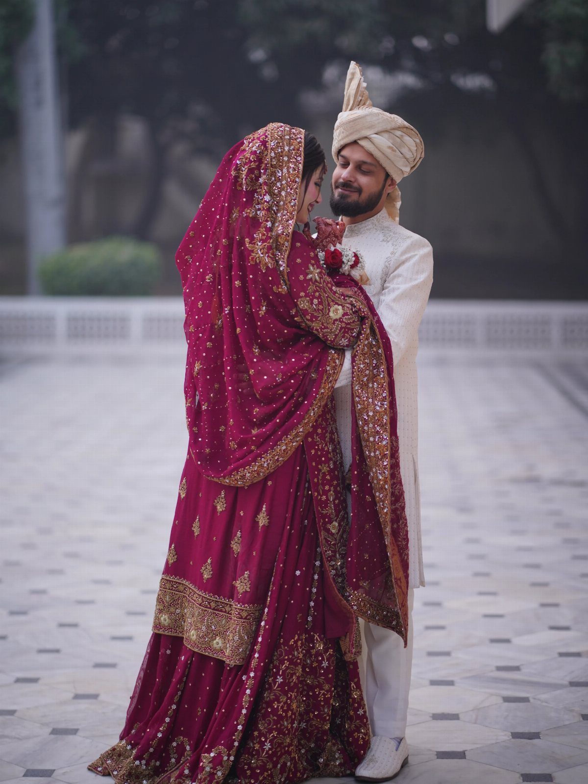 Couple in traditional South Asian wedding attire embracing on a tiled outdoor courtyard.