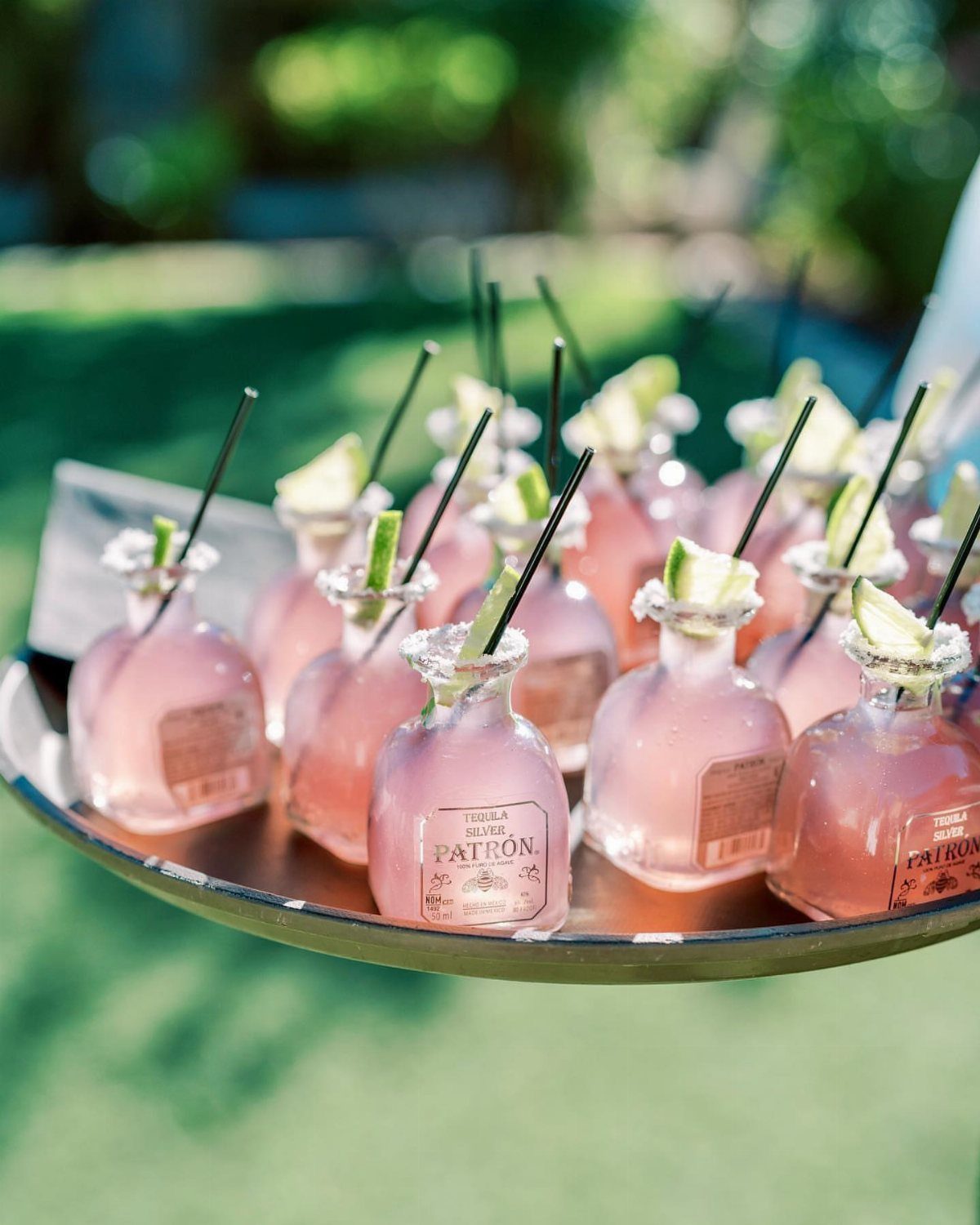 Pink cocktails in small glass bottles with lime wedges on a silver tray.