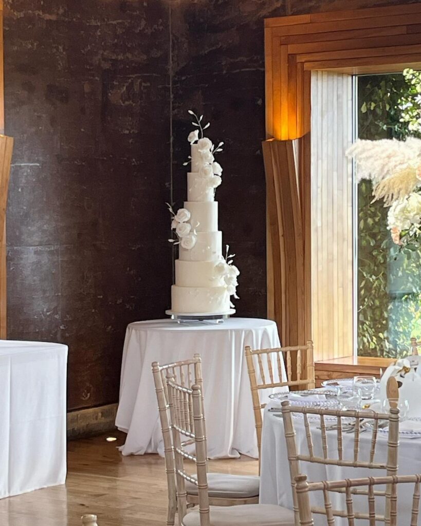 Multi-tiered white wedding cake with floral decorations on a white draped table.