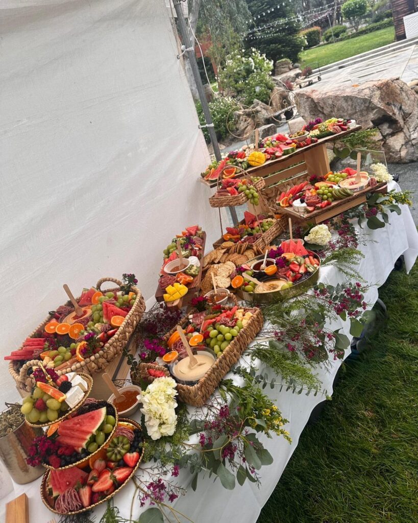 Grazing table with fruit and cheese platters decorated with greenery and white flowers.