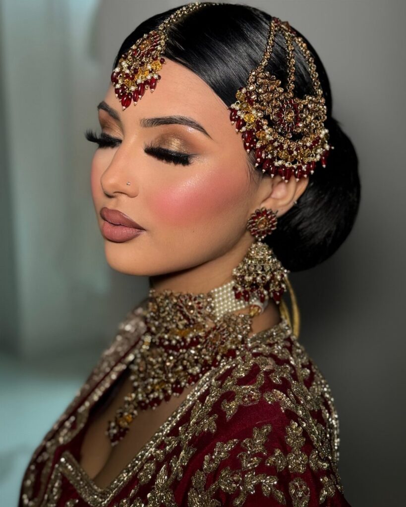 Woman with traditional Indian bridal makeup and gold jewelry wearing a red embroidered outfit