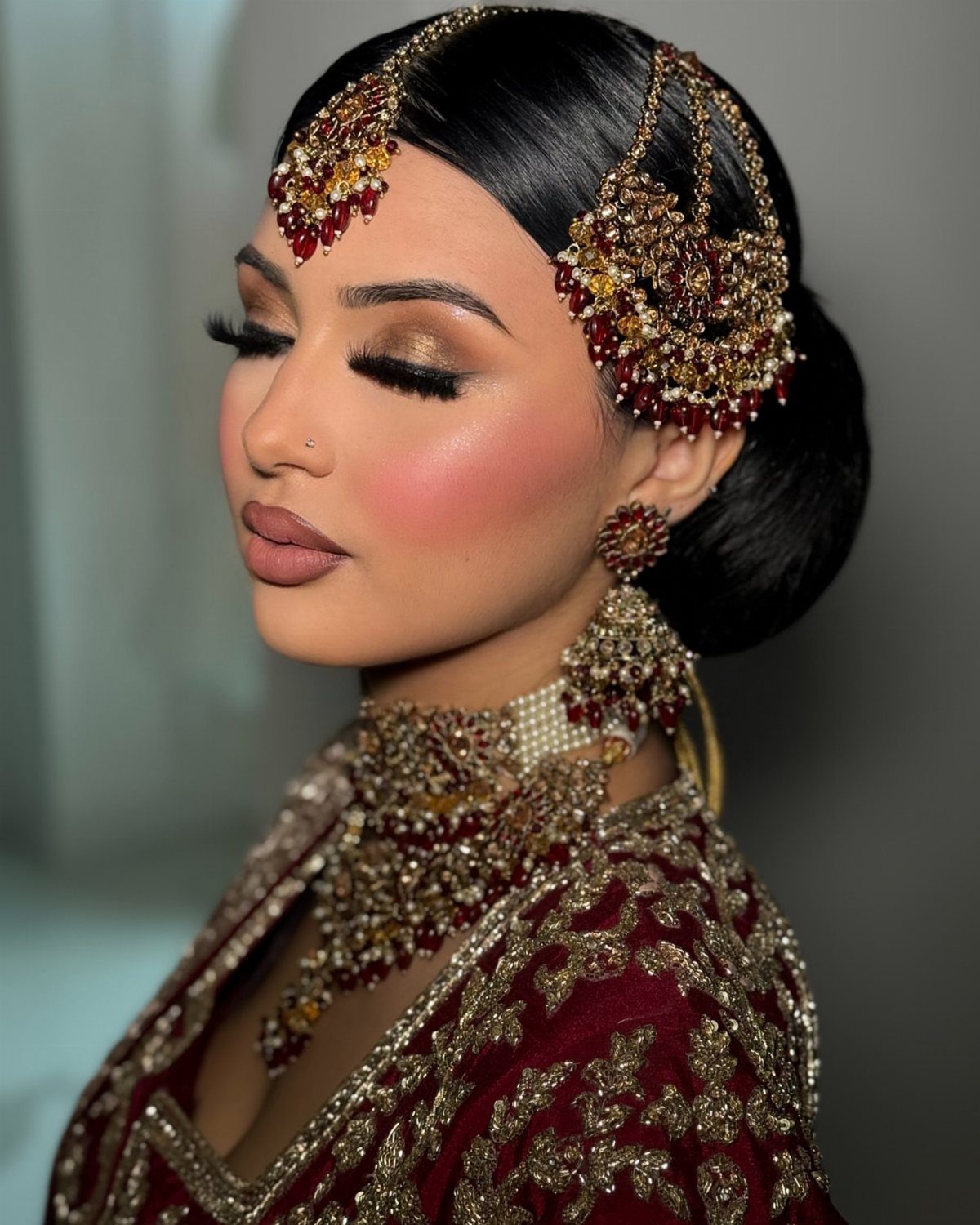 Woman with traditional Indian bridal makeup and gold jewelry wearing a red embroidered outfit