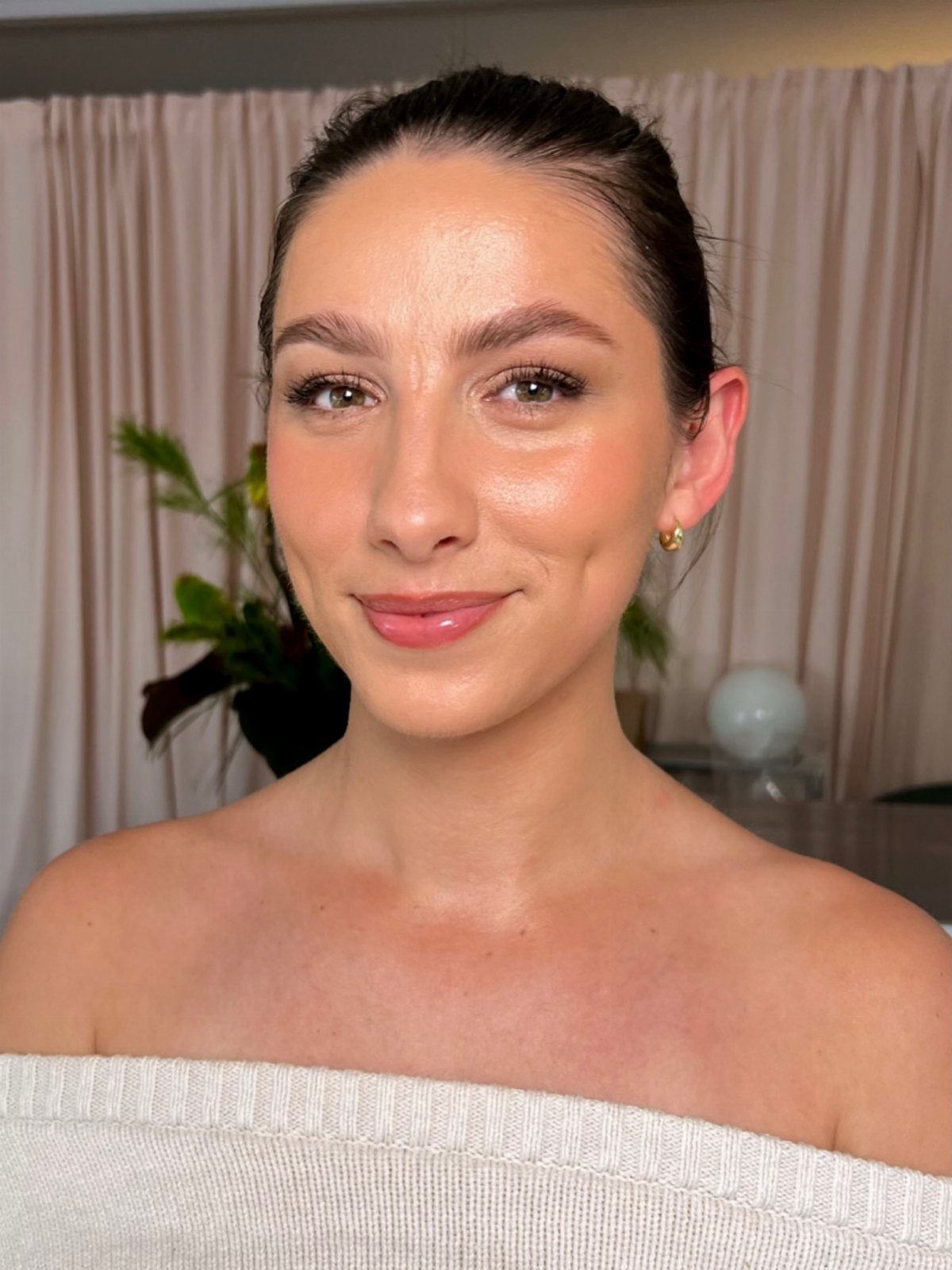 Woman with glowing dewy skin and natural makeup wearing a white off-shoulder top.