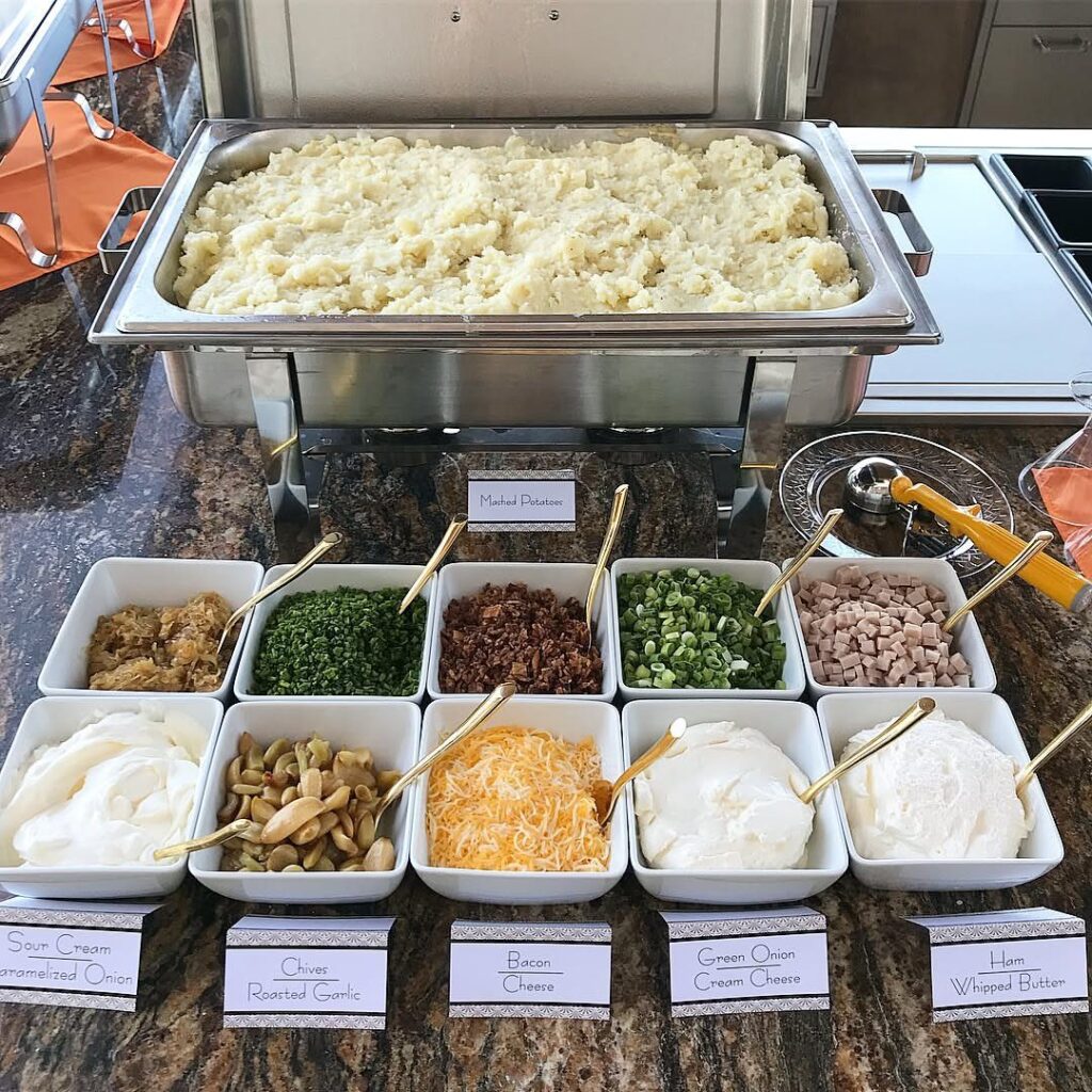 Mashed potato bar with various toppings in white bowls on a granite counter.
