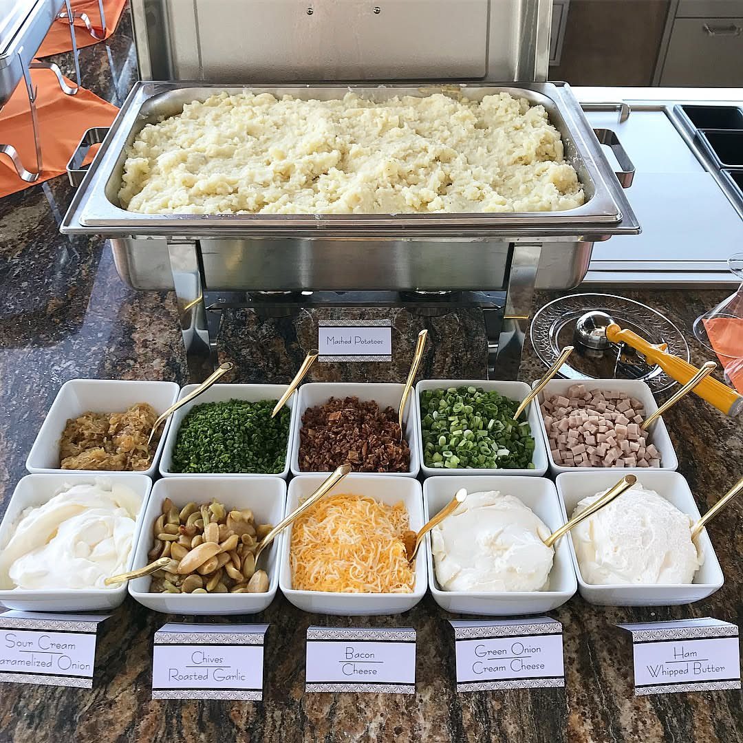 Mashed potato bar with various toppings in white bowls on a granite counter.