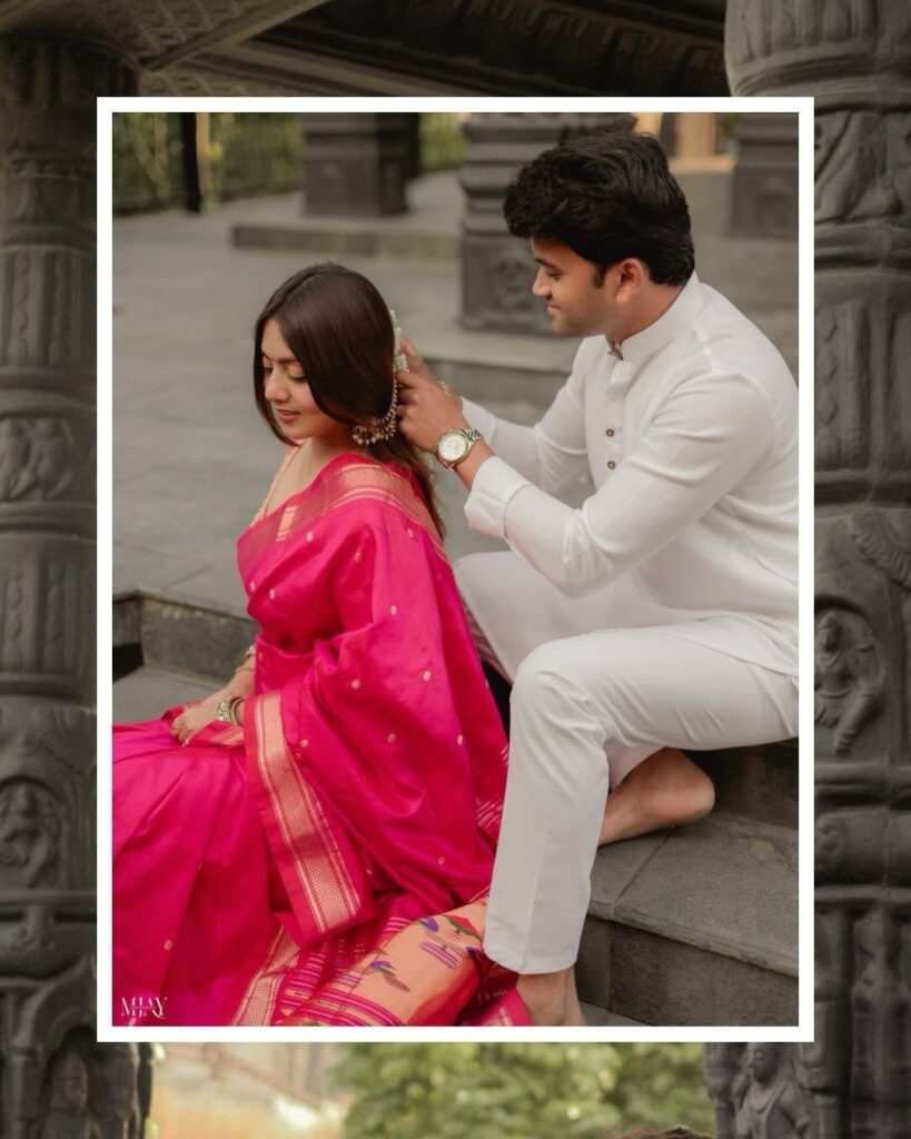 Man in white traditional attire adjusting the earring of a woman in pink saree.