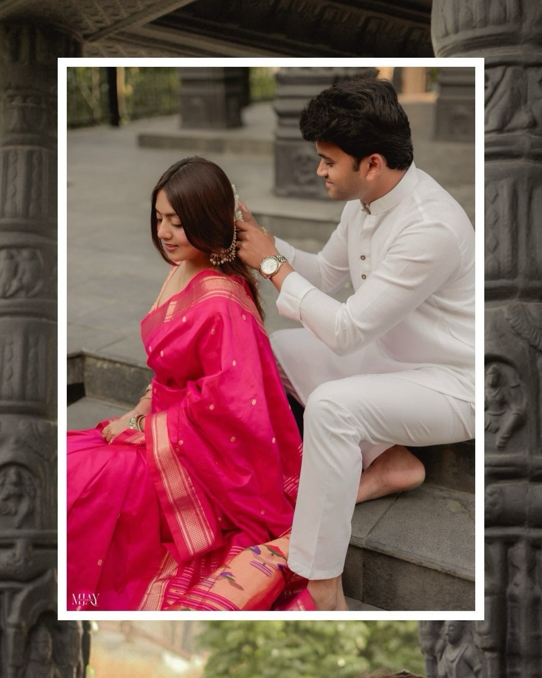 Man in white traditional attire adjusting the earring of a woman in pink saree.