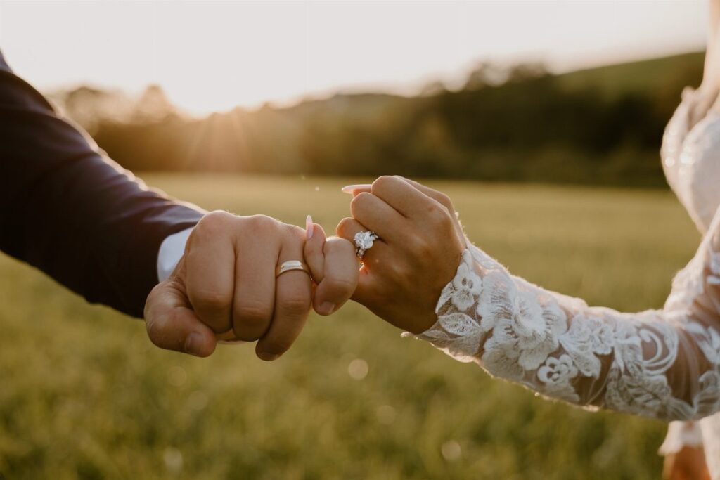 Couple's hands holding each other showing wedding rings in a sunlit grassy field