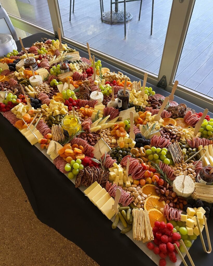 Large charcuterie spread with meats, cheeses, and fruits on a black table.