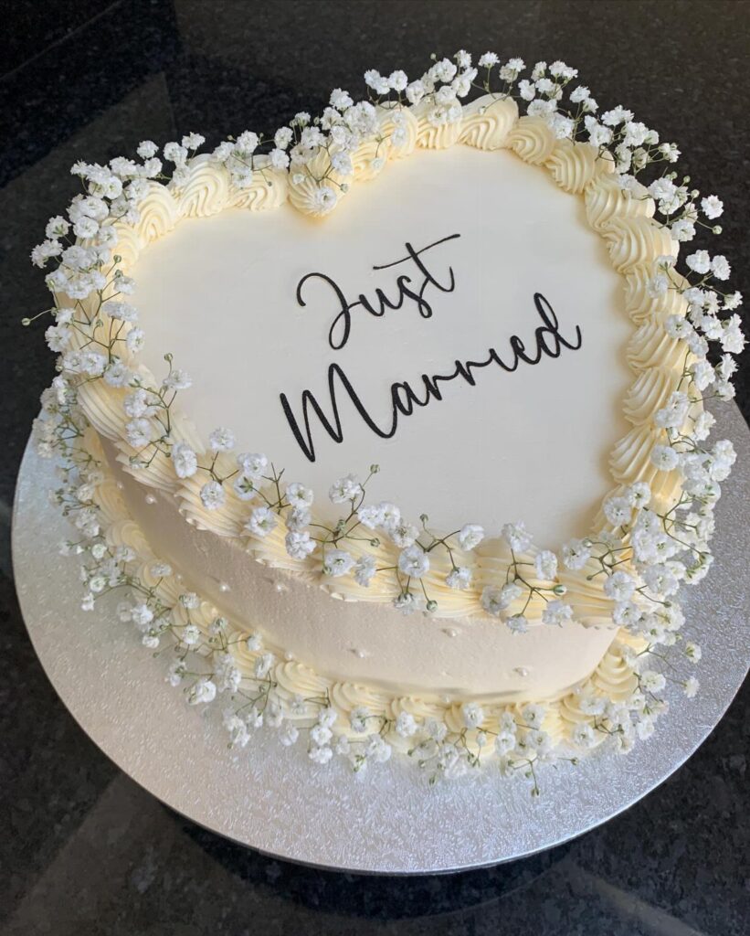 Heart-shaped white wedding cake decorated with baby's breath and Just Married text.