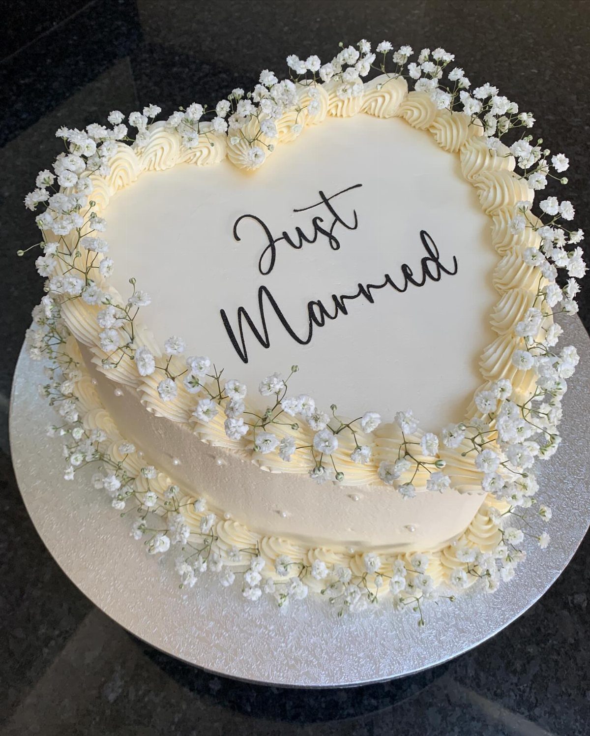 Heart-shaped white wedding cake decorated with baby's breath and Just Married text.