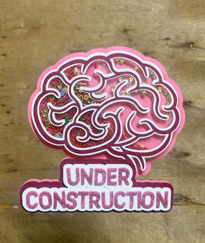 Pink glittery brain cake topper with the words Under Construction on wood.
