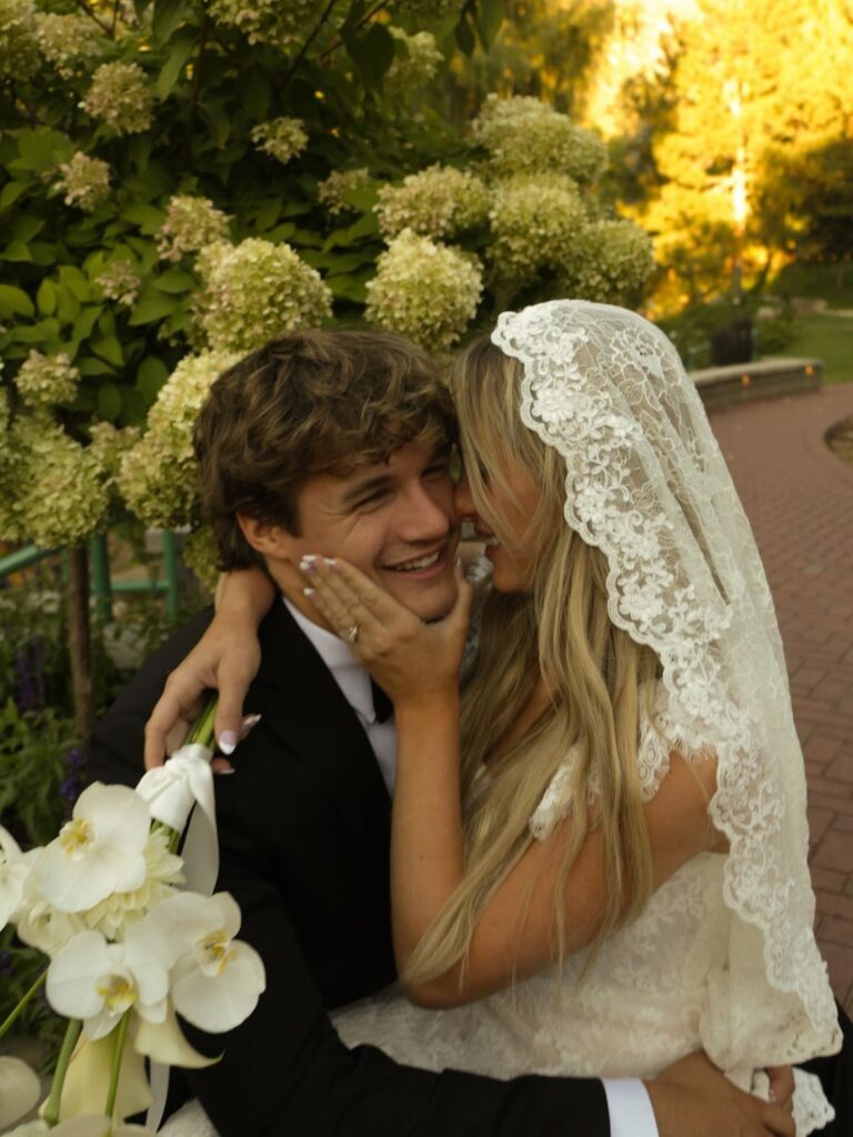 Newlywed couple embracing outdoors with white hydrangeas in the background.