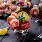 Shrimp cocktail served in glasses with red sauce, lemon slices, and fresh parsley.