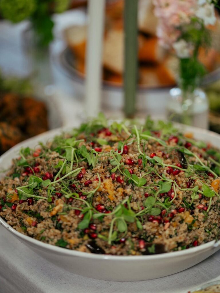 Grain salad with pomegranate seeds and microgreens in a white buffet bowl
