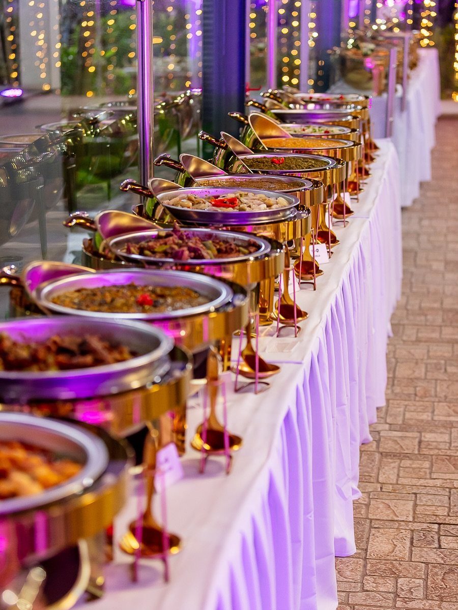 Gold chafing dishes with food on a white tablecloth at a wedding buffet.