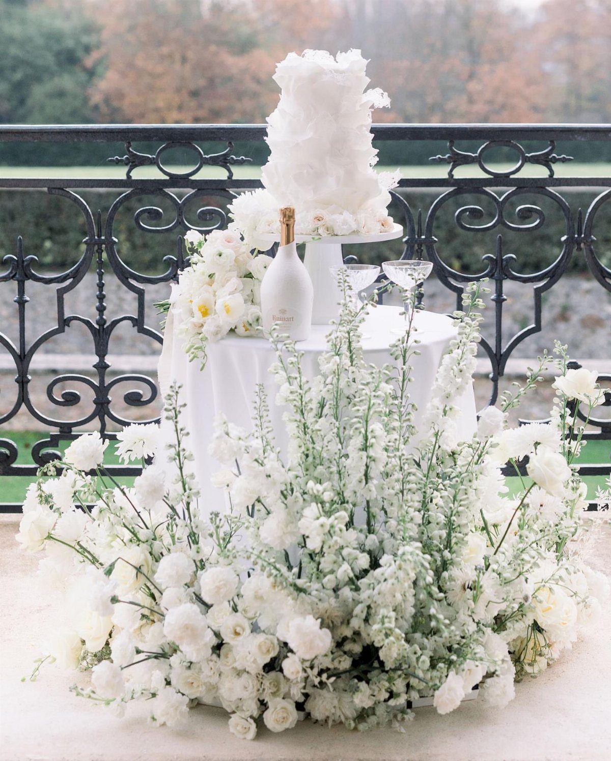 White tiered wedding cake on a flower-decorated table with champagne and glasses.