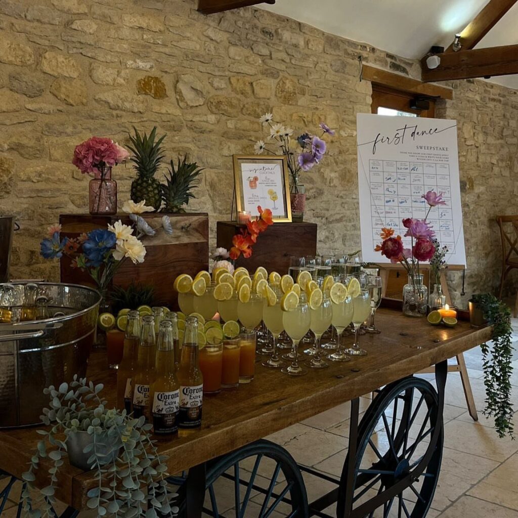 Wooden cart drinks station with cocktails, beer, and flowers against a stone wall