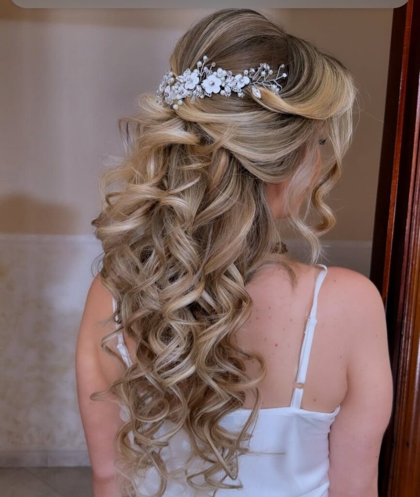 Blonde hair styled in voluminous loose curls with a white floral hair accessory.