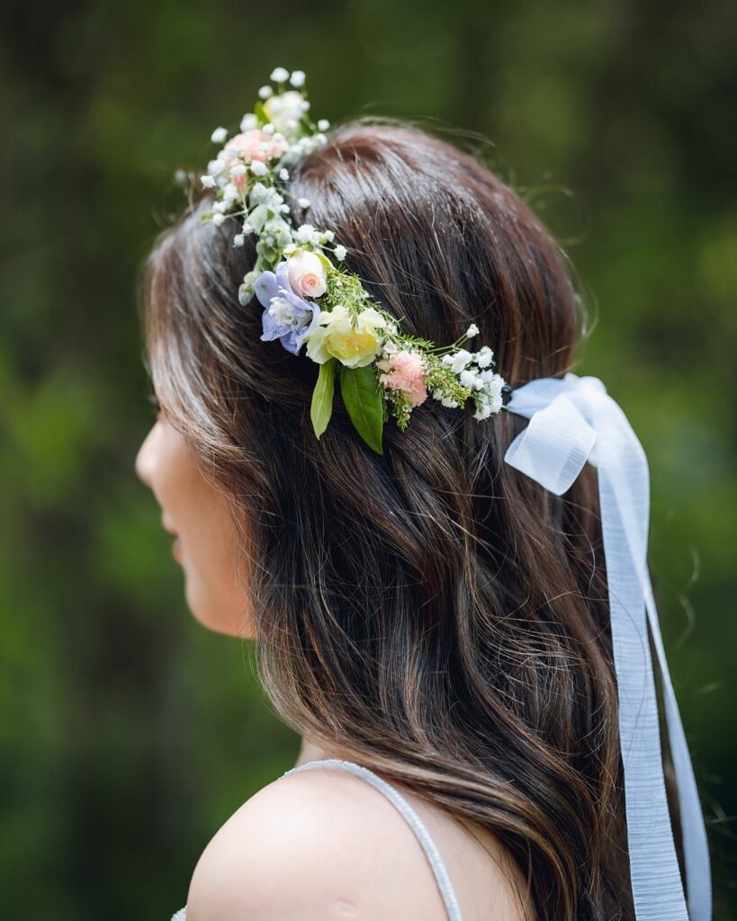Woman wearing a floral crown of white, pink, and blue flowers with ribbon.