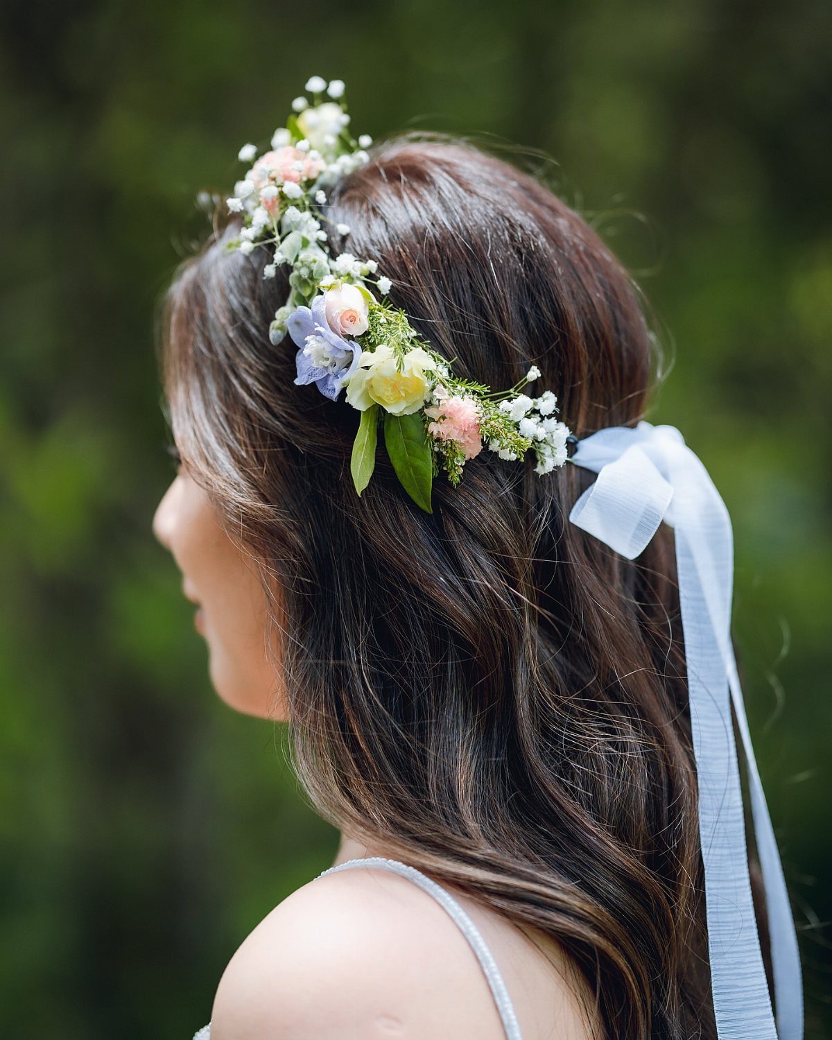 Woman wearing a floral crown of white, pink, and blue flowers with ribbon.