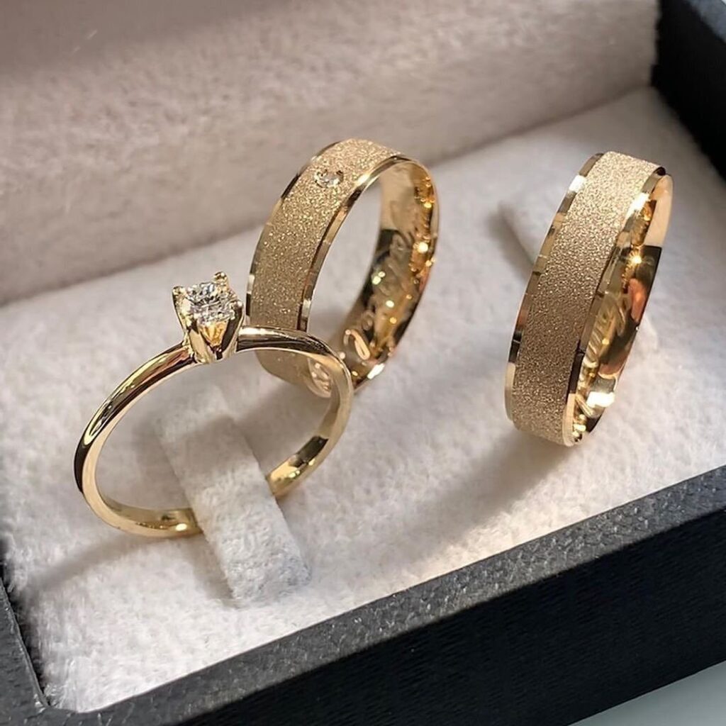 Three gold wedding rings, including a diamond solitaire, in a white velvet box.