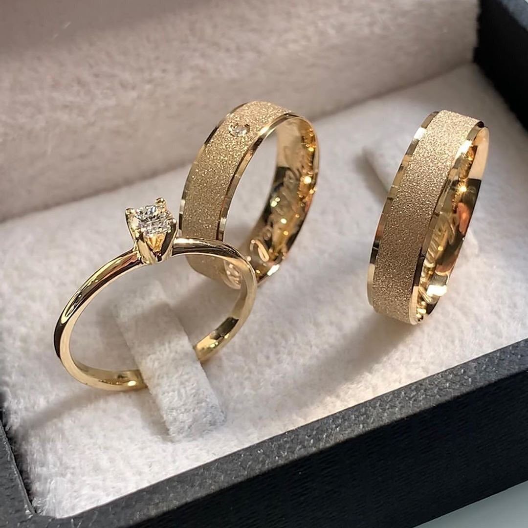 Three gold wedding rings, including a diamond solitaire, in a white velvet box.